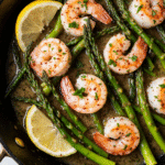 A close-up overhead shot of a black cast-iron skillet filled with a healthy 15-minute meals of garlic shrimp and asparagus, ready to eat.