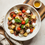 Easy antipasto salad recipe in white bowl with Italian meats, mozzarella cheese, olives and fresh basil